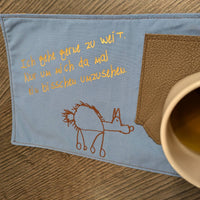 Elegante Plotterdatei von easy-sticks mit dem Spruch 'Ich gehe gerne zu weit. Nur um mich da mal ein bisschen umzusehen.' auf blauem Stoff neben einer Tasse.