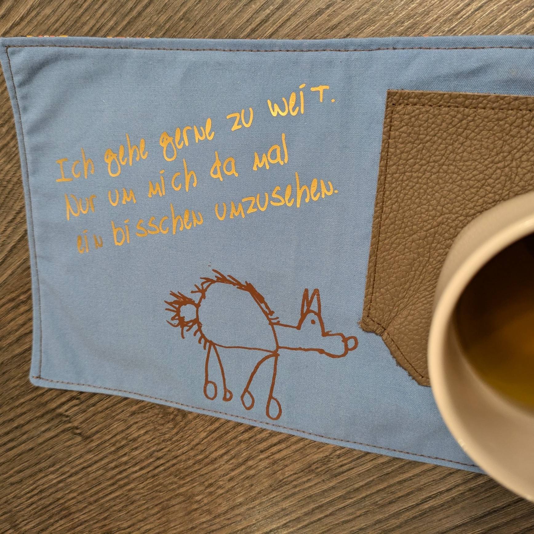 Elegante Plotterdatei von easy-sticks mit dem Spruch 'Ich gehe gerne zu weit. Nur um mich da mal ein bisschen umzusehen.' auf blauem Stoff neben einer Tasse.