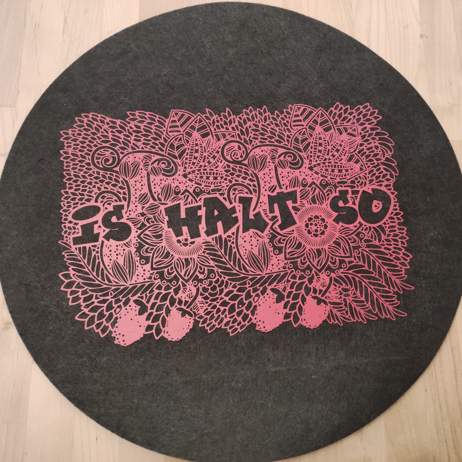 Kreatives Design mit der 'Is halt so' Plotter Datei von easy-sticks. Die pinkfarbene Lasergravur zeigt florale Motive und den Schriftzug 'Is halt so' auf einem runden, grauen Untergrund, ideal für individuelle Bastelprojekte.