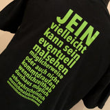 Schwarzes T-Shirt mit dem Aufdruck "JEIN vielleicht kann sein zu eventuellem Malsehen" in leuchtendem Grün, entworfen von easy-sticks. Ein kreatives Kleidungsstück für humorvolle Anlässe.