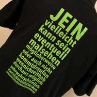 Schwarzes T-Shirt mit dem Aufdruck "JEIN vielleicht kann sein zu eventuellem Malsehen" in leuchtendem Grün, entworfen von easy-sticks. Ein kreatives Kleidungsstück für humorvolle Anlässe.