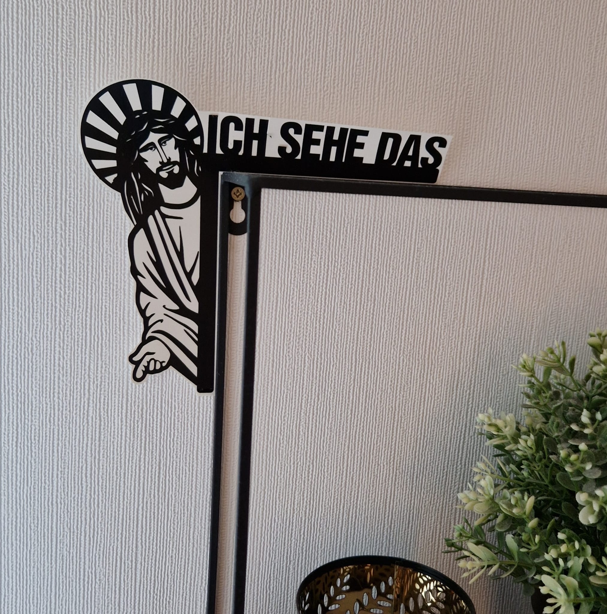 Dekoratives Wandobjekt "Jesus, ich sehe das" von easy-sticks, das auf einem Spiegel sitzt, umgeben von einem Topf mit Pflanzen, in stilvollem, modernem Design.