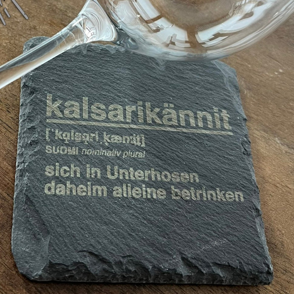 Kreatives Kalsarikännit Design von easy-sticks: Eine elegante Glaskelch und ein gravierter Stein mit dem Wort "kalsarikännit" auf einem Holzuntergrund, ideal für DIY-Projekte.