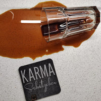 Kaffeeglas umgekippt auf einem Tisch mit dem Untersetzer 'KARMA Schätzchen', erhältlich bei easy-sticks.