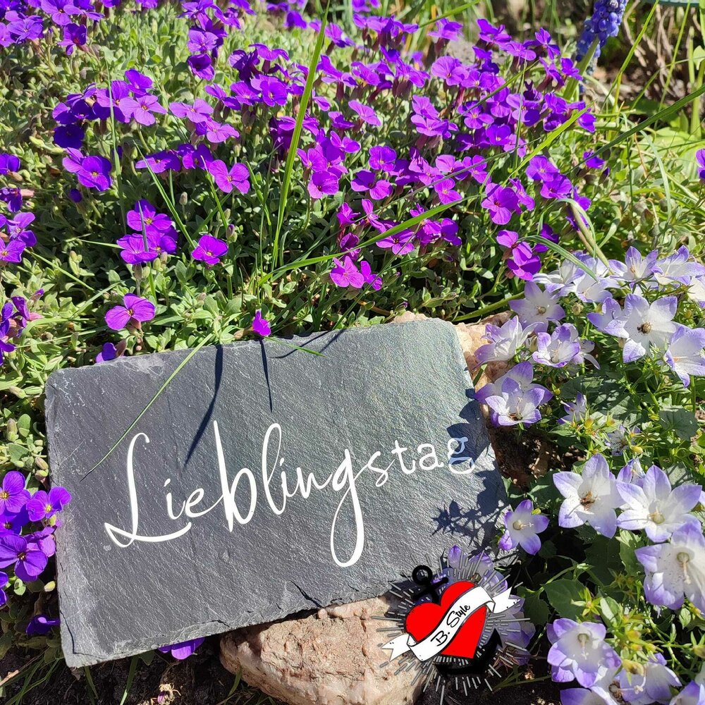 Ein stilvoller Schieferstein mit dem Schriftzug "Lieblingstag" umrahmt von lila und weißen Blumen, perfekt für besondere Anlässe, entstanden mit der Plotterdatei "Kerzensprüche für jeden Anlass 2" von easy-sticks.