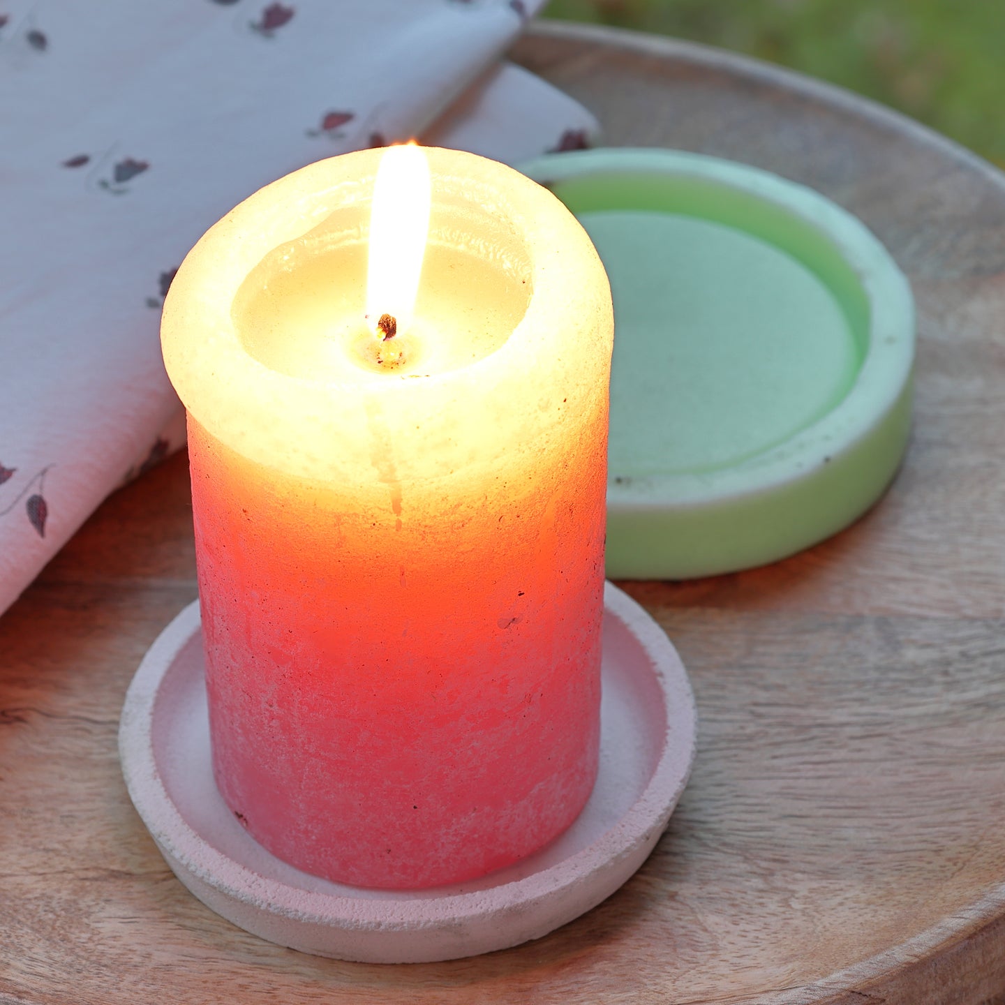 Runder Kerzenständer Silikonform von easy-sticks mit einer leuchtenden, brennenden Kerze in Orangetönen, begleitet von einer grünen Silikonform auf einem Holzuntergrund.
