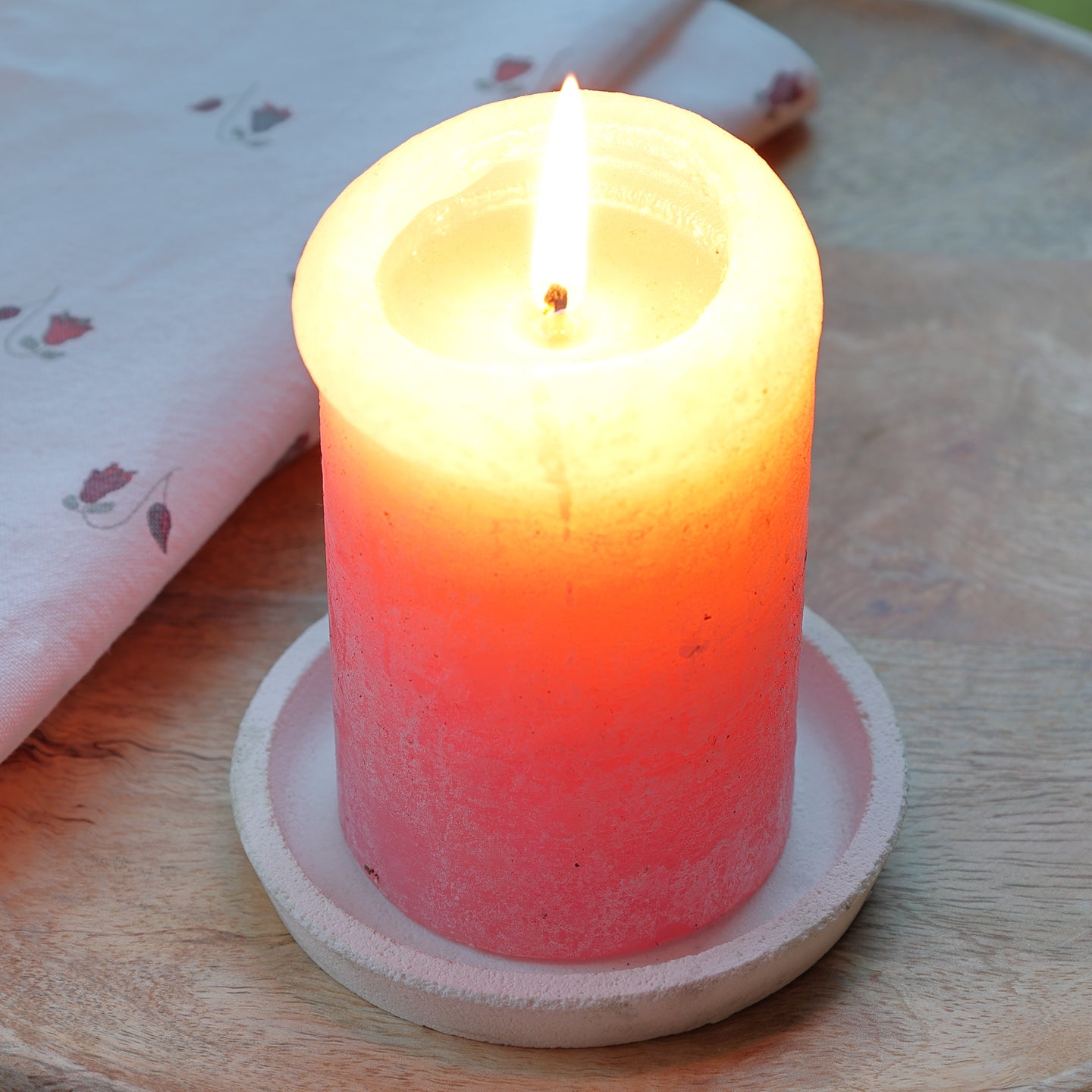 Runder Kerzenständer Silikonform von easy-sticks mit einem brennenden kerzenförmigen Element in Orange, das auf einem rustikalen Holzbrett steht, umgeben von einem bedruckten Tuch.