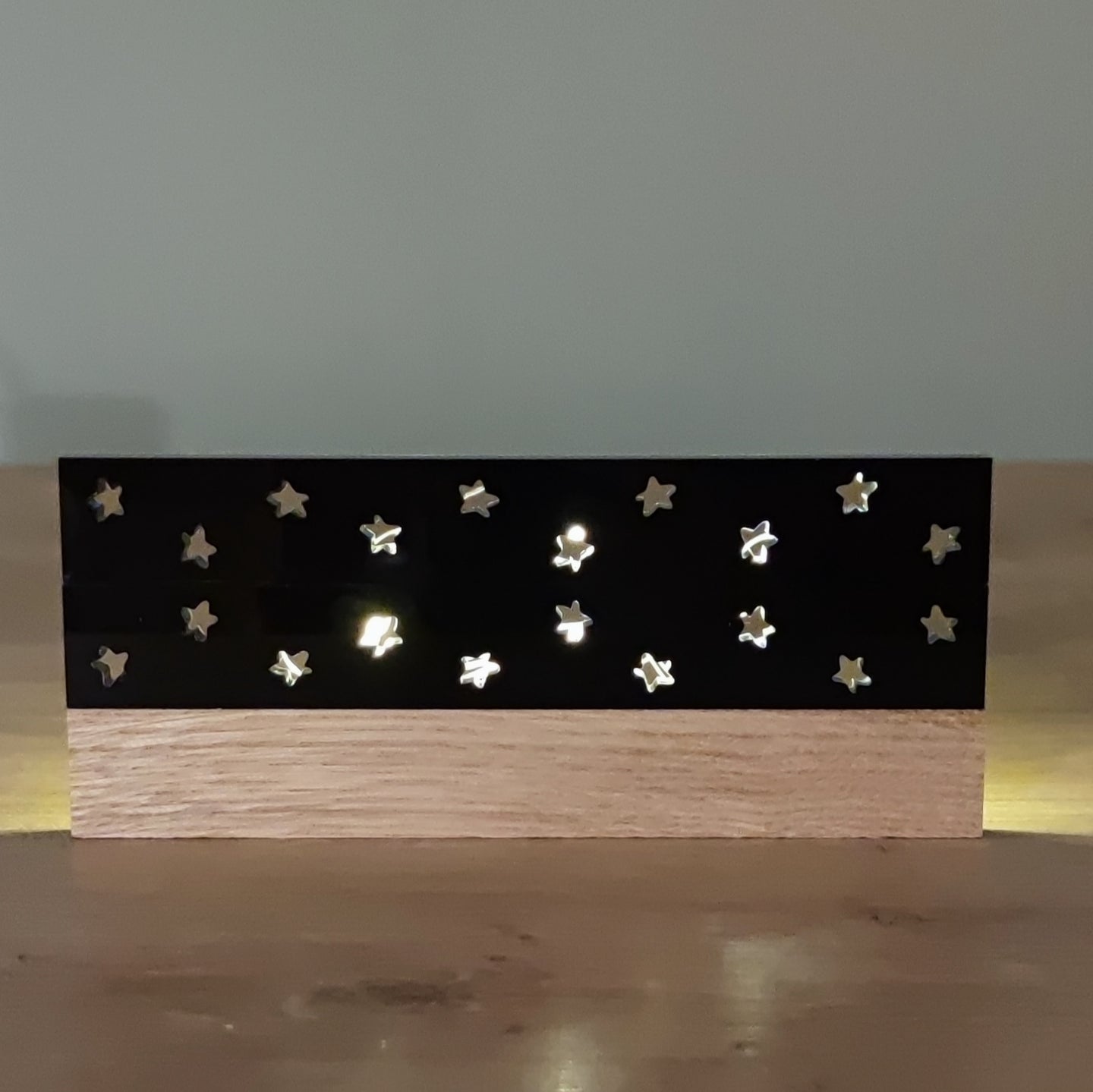 Schwarze Acrylstern-Platte von Easy-Sticks, die an einer Holzunterlage angebracht ist. Die hochglänzende Oberfläche ist mit ausgefrästen Sternen dekoriert, die Licht durchscheinen lassen. Ideal für stimmungsvolle Dekorationen.