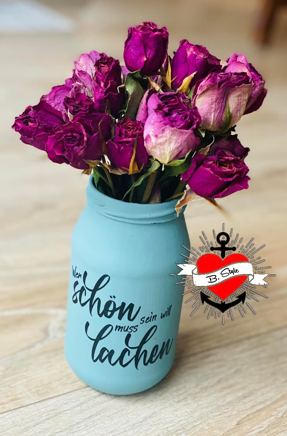 Vase in Blau mit getrockneten Rosen und dem Schriftzug "Wer schön sein will muss lachen" von easy-sticks, perfekt für die Verschönerung von Wohnräumen.