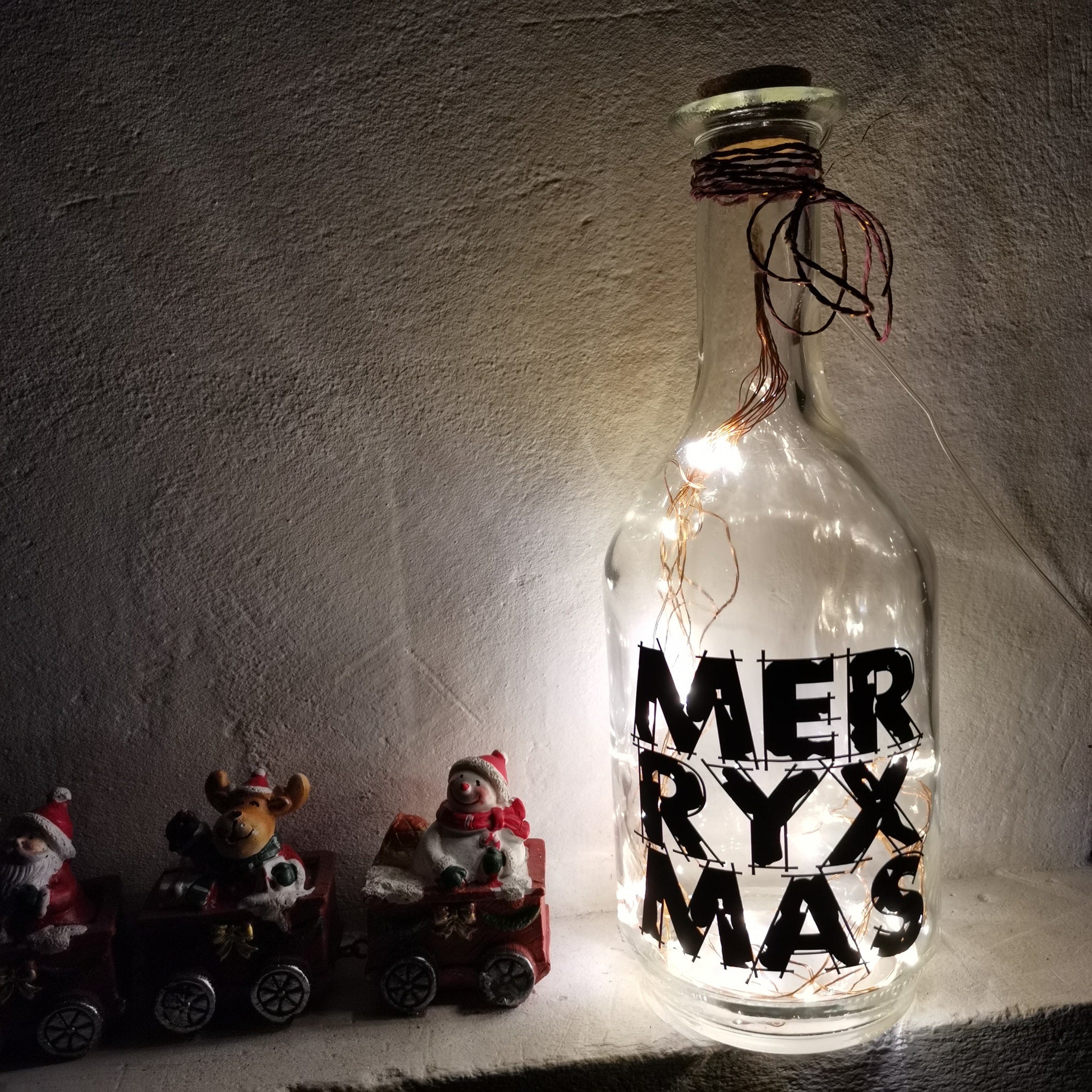Dekorative Glasflasche mit Lichtern und dem Schriftzug 'MERRY X MAS', gestaltet mit der 'Merry X Mas' Plotterdatei von easy-sticks, ideal für festliche Kreativprojekte.