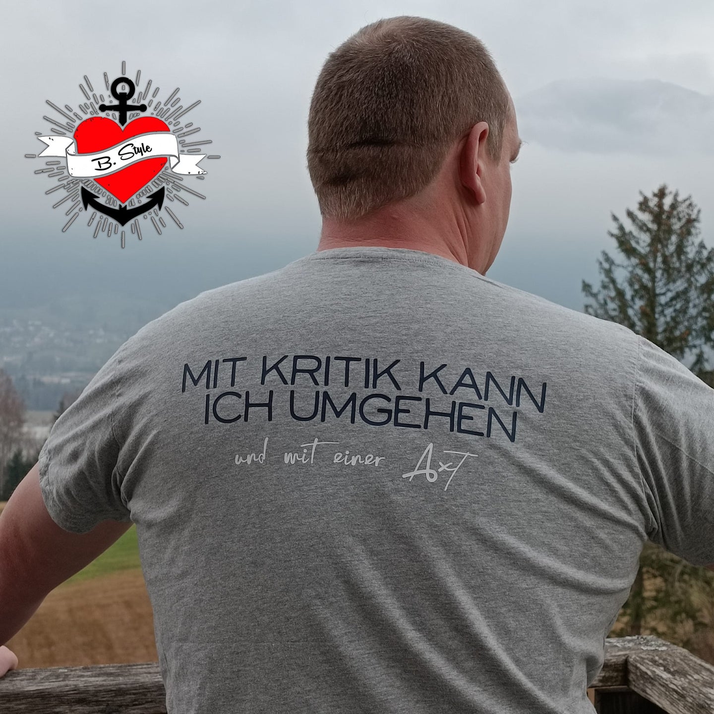 Mann mit grauem T-Shirt, das das Design "Mit Kritik kann ich umgehen - und mit einer Axt" trägt. Perfekt für persönliche DIY-Ideen mit der Plotterdatei von easy-sticks.