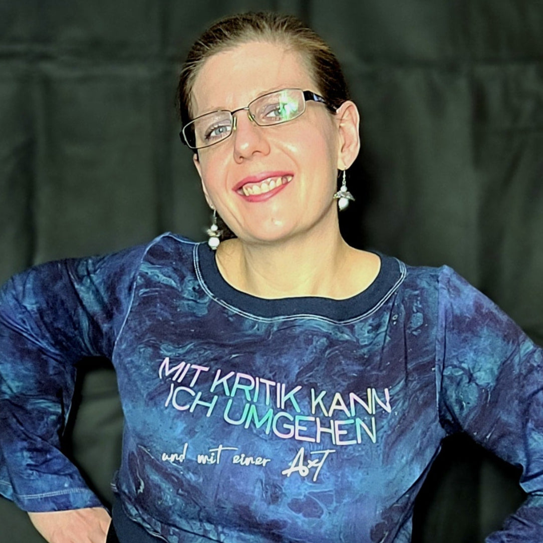 Person in blauer Kleidung, die ein Sweatshirt mit dem Aufdruck "Mit Kritik kann ich umgehen - und mit einer Axt" trägt. Von easy-sticks, ideal für individuelle Designs mit einer Plotterdatei.