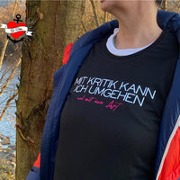 Frau in schwarz-blauem Outfit mit T-Shirt, das das Design "Mit Kritik kann ich umgehen - und mit einer Axt" zeigt. Eine schöne Inspiration für kreative Arbeiten mit der Plotterdatei von easy-sticks.
