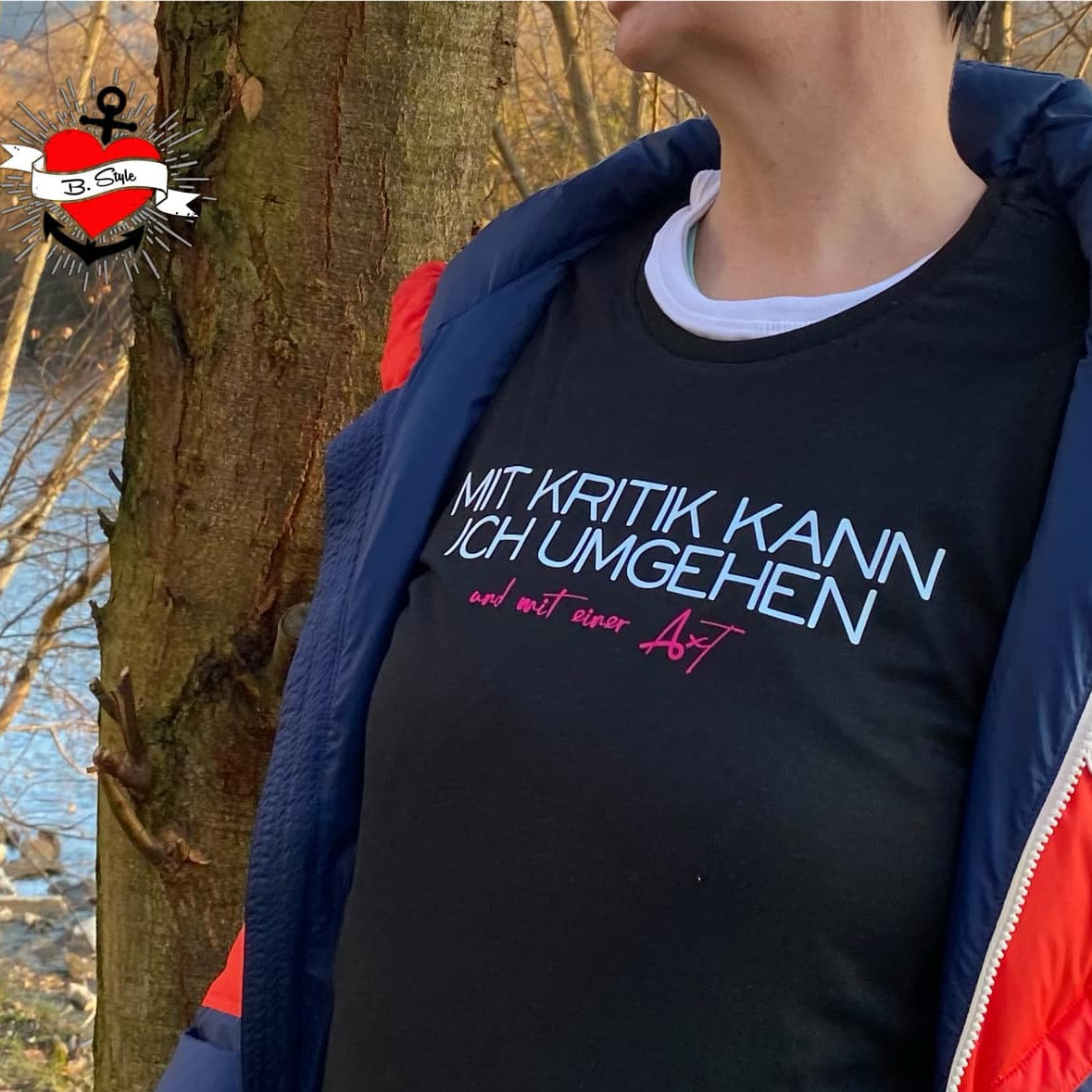 Frau in schwarz-blauem Outfit mit T-Shirt, das das Design "Mit Kritik kann ich umgehen - und mit einer Axt" zeigt. Eine schöne Inspiration für kreative Arbeiten mit der Plotterdatei von easy-sticks.