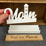 Easy-Sticks Einschieber Silikonform - Moin Leuchtturm, ein Handmodell zeigt den weißen Schriftzug 'Moin' vor einer Holzablage mit einer persönlichen Botschaft.