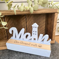 Fertiggestellter Easy-Sticks Einschieber - Moin Leuchtturm auf einem Holzregal dekoriert, mit der Aufschrift 'Der Strand ruft', perfekt für individuelle Geschenkideen.