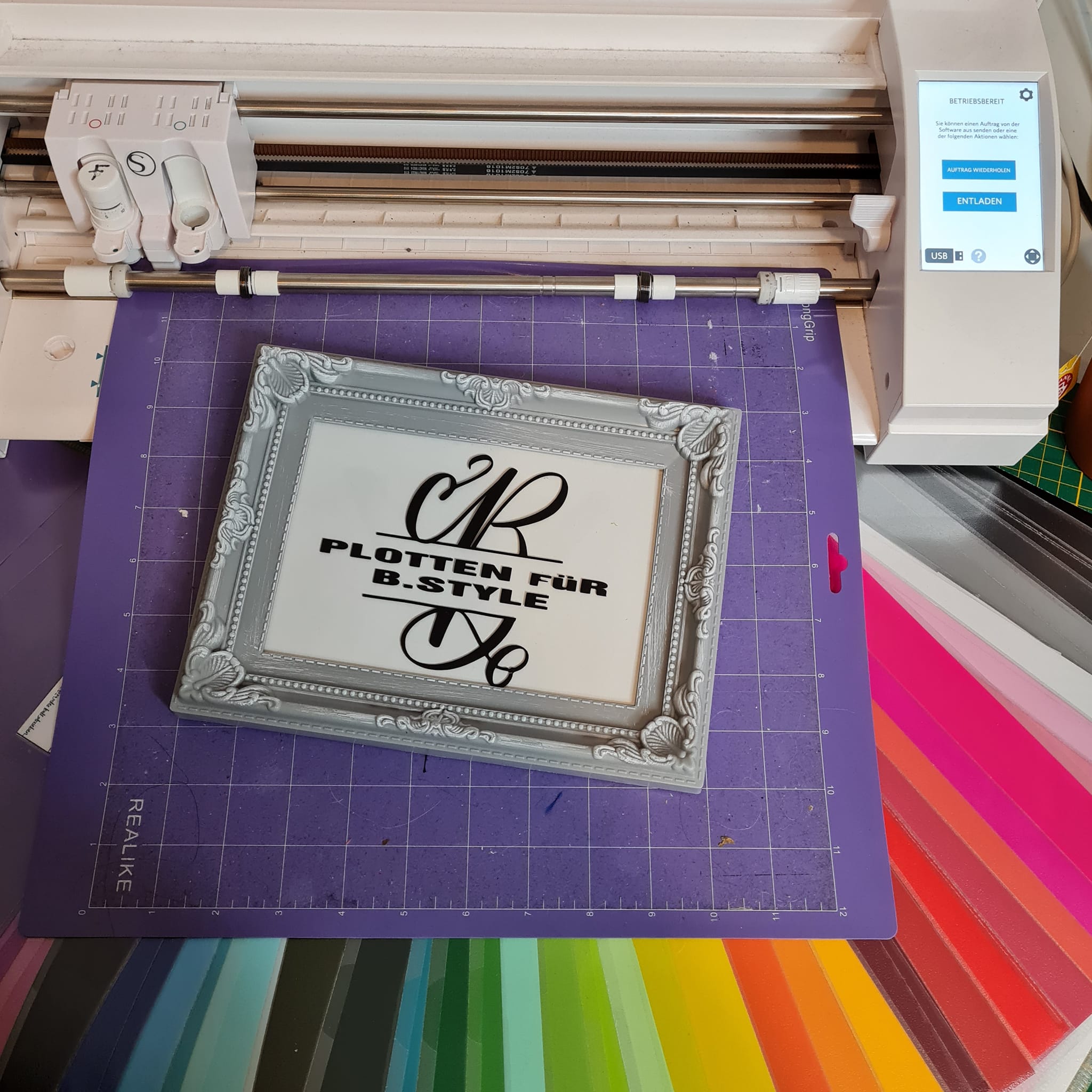 Laser Schneidmaschine, die eine dekorative Tafel mit dem Text 'PLOTTEN FÜR B.STYLE' anzeigt, produziert mit der Monogram 'B' Plotterdatei von easy-sticks.