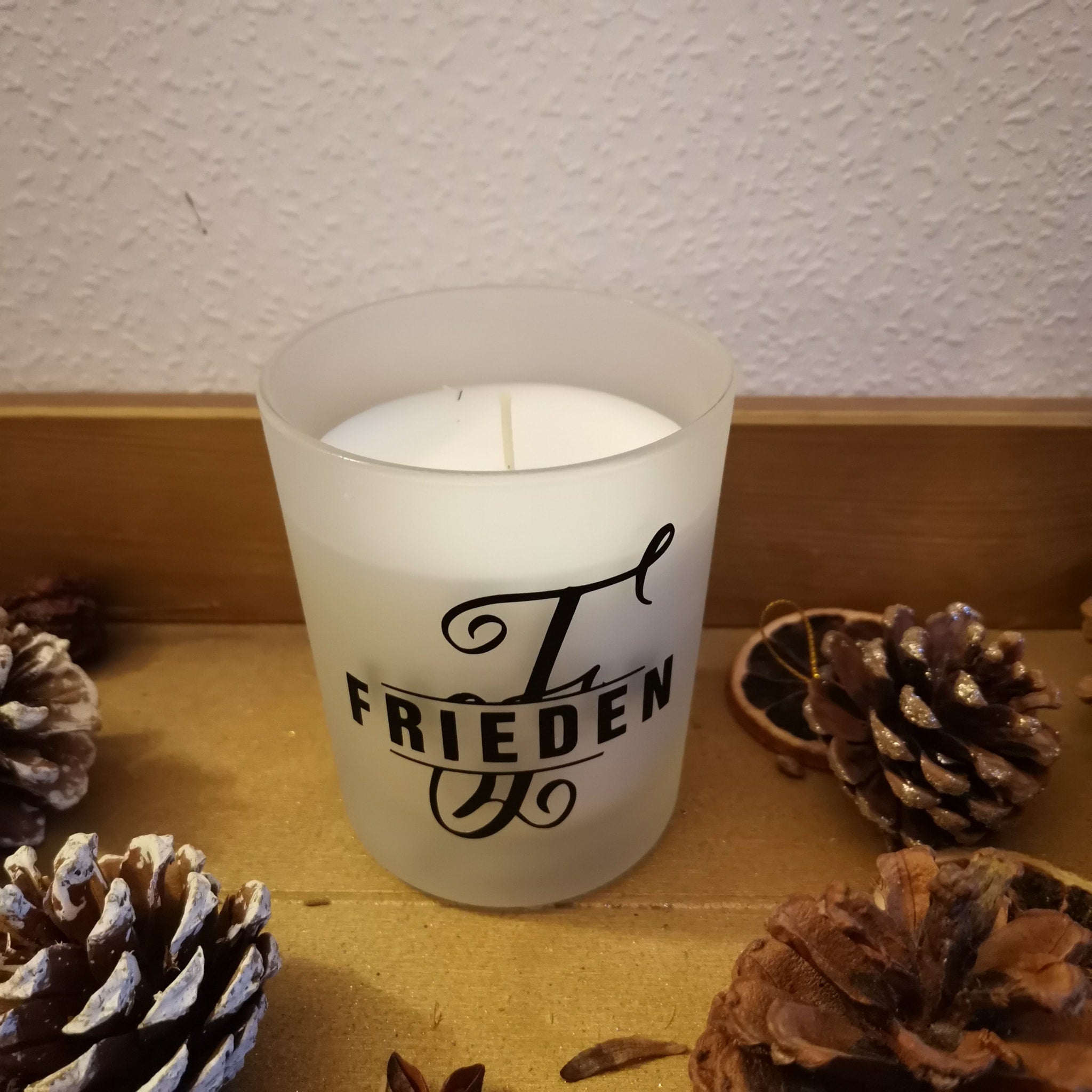 Ein stilvolles Kerzenglas verziert mit dem Monogramm 'F' aus der Plotterdatei von easy-sticks, begleitet von natürlichen Dekorationselementen wie Tannenzapfen.