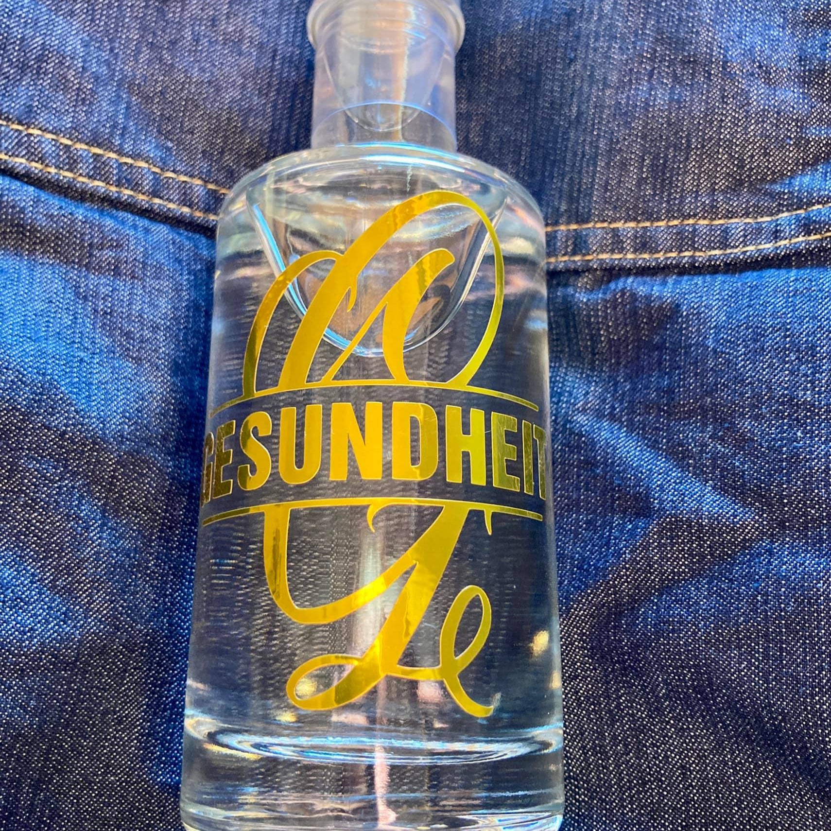 Eine Flasche mit einem Aufkleber, der das Wort 'GESUNDHEIT' zusammen mit dem Monogram 'G' anzeigt. Ideal für kreative Geschenkideen, entworfen mit der Monogram 'G' Plotterdatei von easy-sticks.