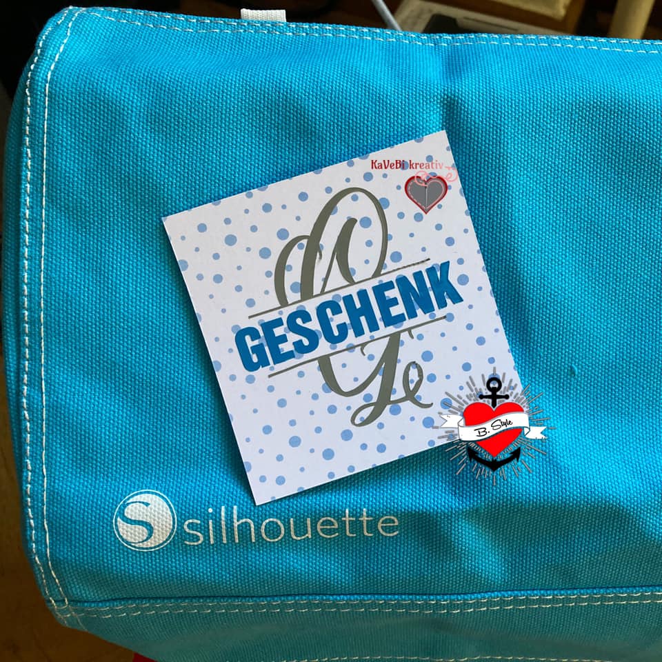 Eine blaue Tasche mit einem Geschenk, das eine Karte mit der Aufschrift 'GESCHENK' trägt. Perfekt für kreative Bastelideen, inspiriert von der Monogram 'G' Plotterdatei von easy-sticks.