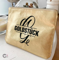 Monogramm 'G' Plotterdatei von easy-sticks, goldene Kosmetiktasche mit dem Aufdruck GOLDSTÜCK und künstlerischem Buchstaben G in schwarz.