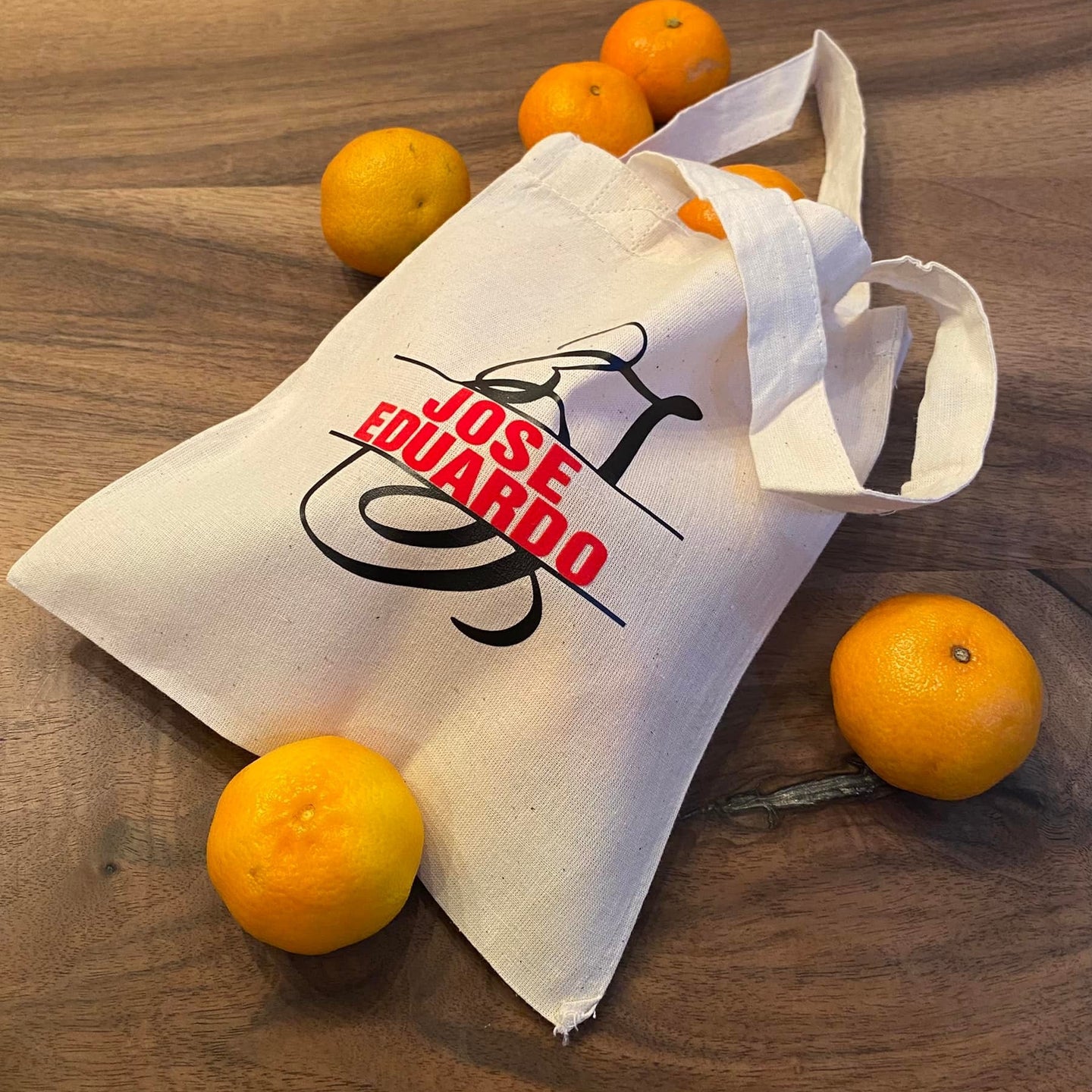 Monogramm 'J' Plotterdatei von easy-sticks auf einer Stofftasche, beschriftet mit 'JOSE EDUARDO', umgeben von frischen Orangen. Perfekt für personalisierte Geschenke.