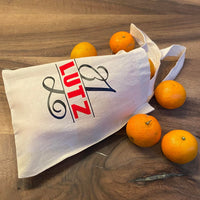 Benutzerdefinierte Tragetasche mit dem Monogramm "L" von easy-sticks, dekoriert mit roten und schwarzen Buchstaben, umgeben von frischen, orangefarbenen Früchten.