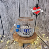 Schlichtes Glas mit einer Kerze und dem Monogramm "L" aus der Plotterdatei von easy-sticks, personalisiert mit dem Namen "LEA", auf einem rustikalen Holzring, ideal für persönliche Geschenke.