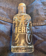 Elegante Flasche mit eingraviertem Text "MERCI" und dem Monogram "M" Plotterdatei von easy-sticks, dargestellt auf blauer Jeansstoff.
