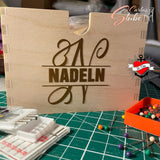 Monogramm 'N' Plotterdatei von easy-sticks, präsentiert auf einer Holzbox für Nadeln, umgeben von Nähzubehör.