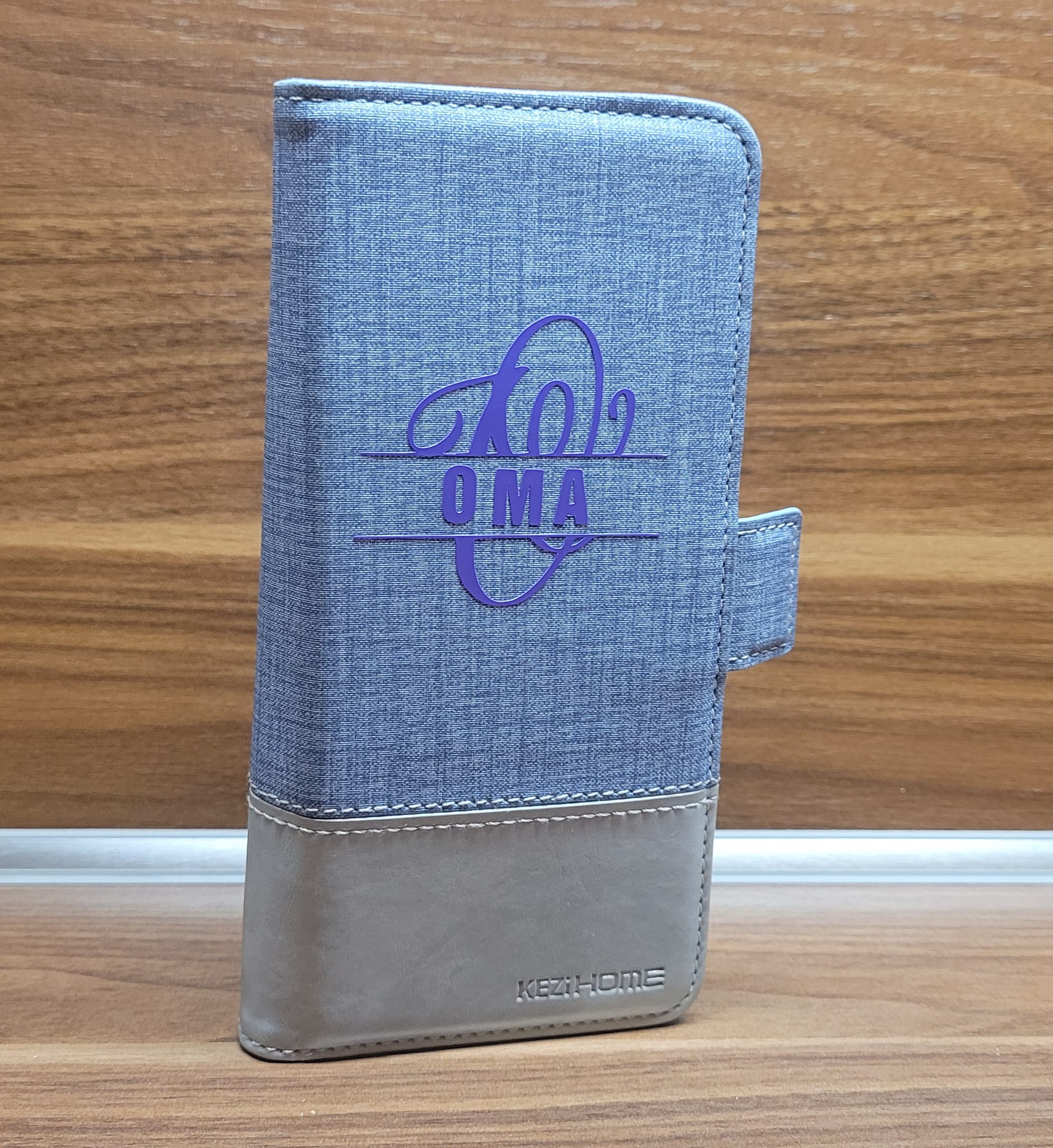 Elegante Brieftasche mit Monogramm "O" Plotterdatei von easy-sticks, personalisiert mit dem Wort "OMA" in lila auf einem grauen Textil-Material.