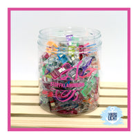 Bunte Stoffklammern in einem transparenten Behälter, ideal für kreative Projekte mit der Monogram 'S' Plotterdatei von easy-sticks. Perfekt zum Halten von Stoffen beim Nähen.