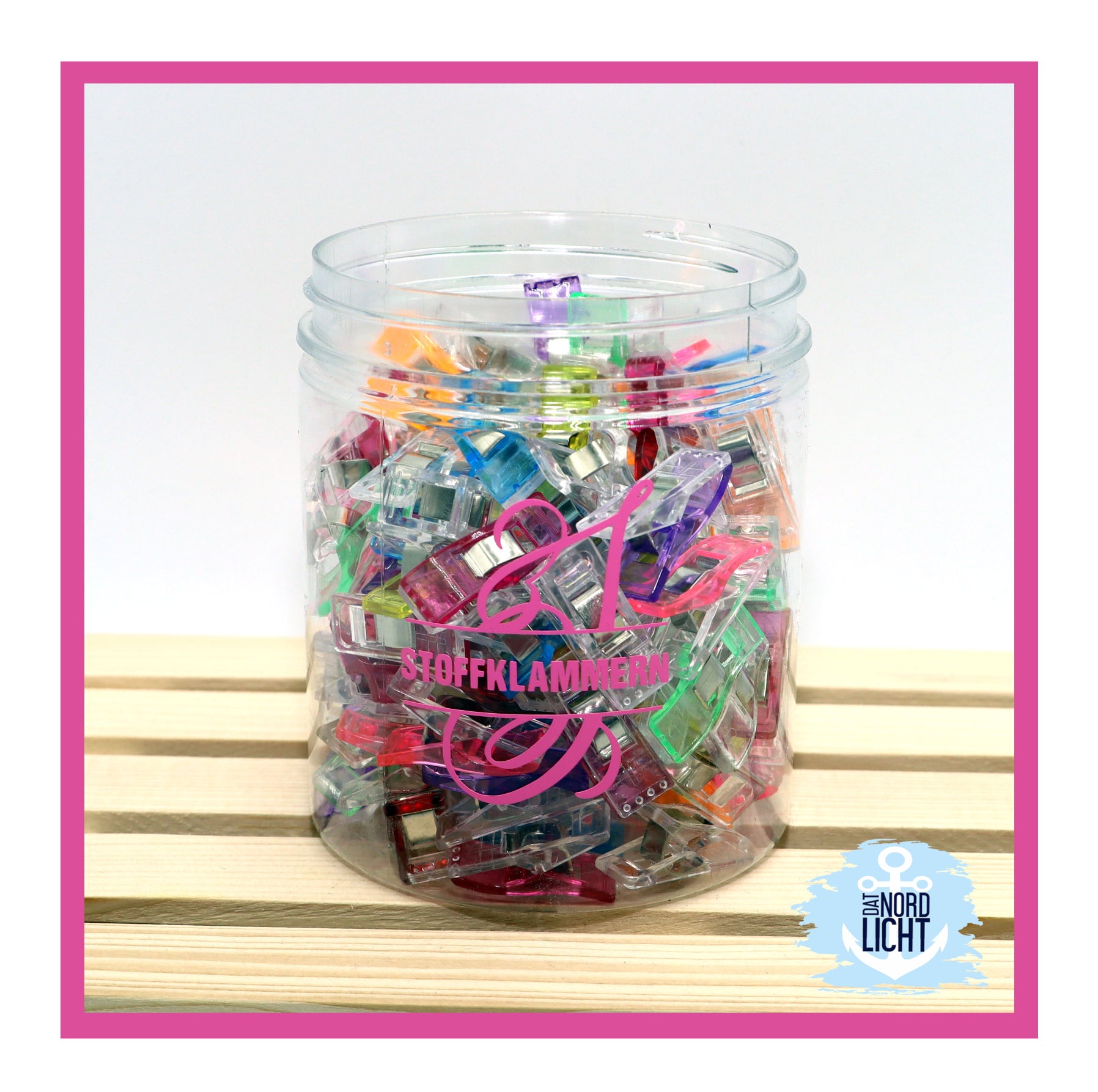 Bunte Stoffklammern in einem transparenten Behälter, ideal für kreative Projekte mit der Monogram 'S' Plotterdatei von easy-sticks. Perfekt zum Halten von Stoffen beim Nähen.