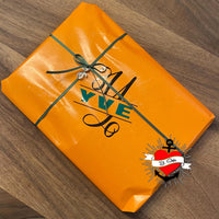 Ein kunstvoll verpacktes Geschenk in orange mit grüner Schleife, geeignet für besondere Anlässe, inspiriert von der Monogram 'Y' Plotterdatei von easy-sticks.