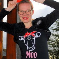 Junge Frau mit einer roten Schleife im Haar, die ein schwarzes T-Shirt mit einem Kuh-Design und dem Schriftzug 'MOO' trägt, entworfen von easy-sticks.