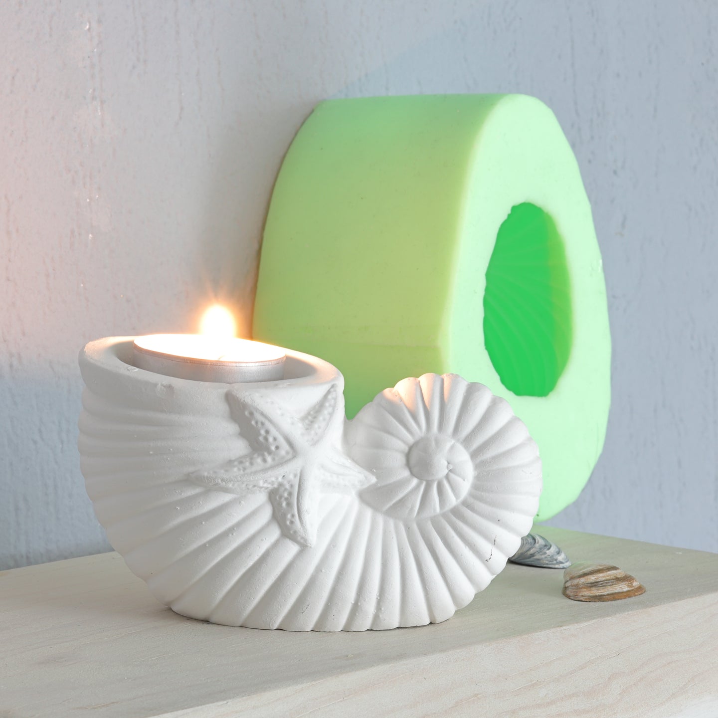 Eleganter Teelichthalter in Muschelform aus hochwertigem Silikon von easy-sticks, beleuchtet mit einer Kerze und umgeben von kreativen Bastelmaterialien.