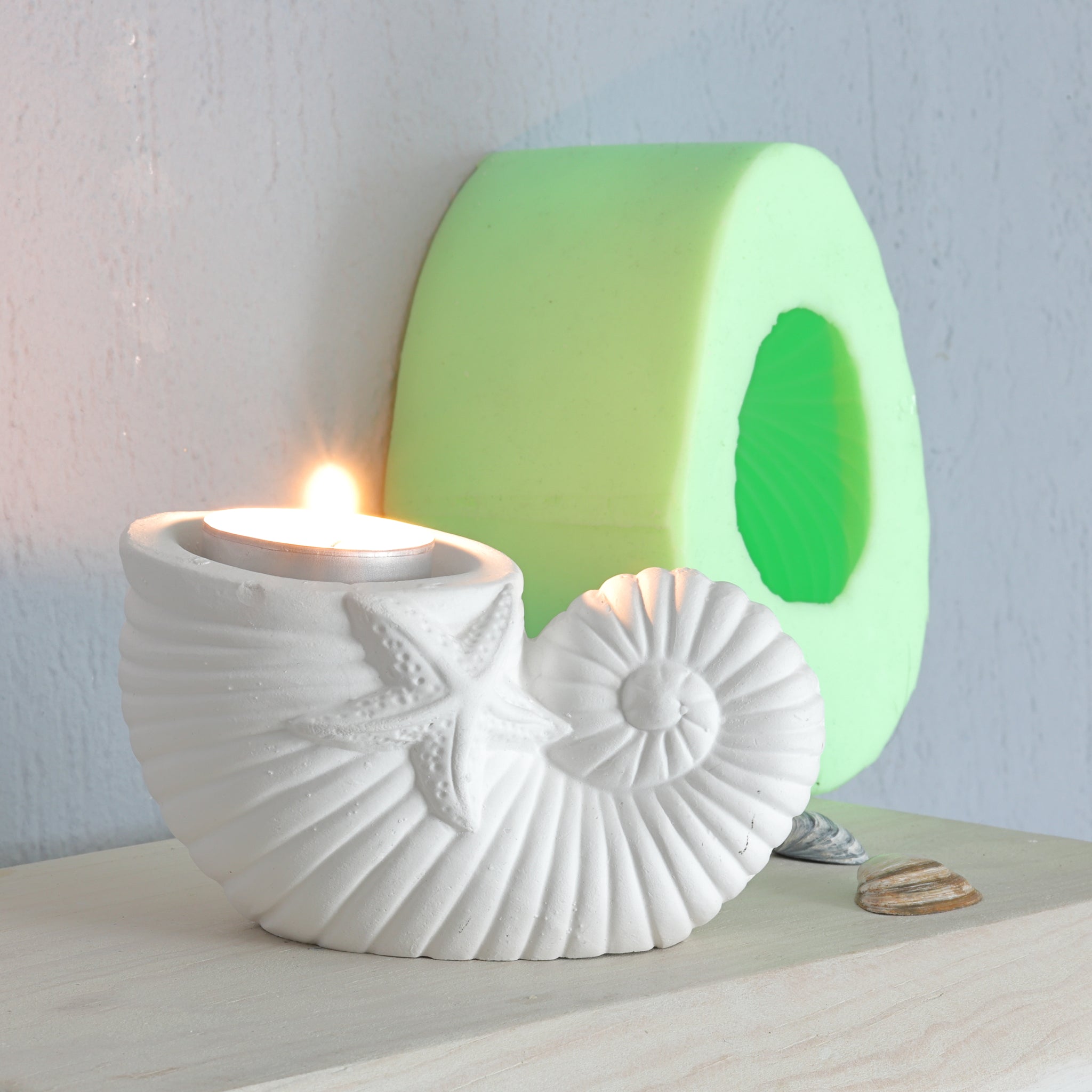 Eleganter Teelichthalter in Muschelform aus hochwertigem Silikon von easy-sticks, beleuchtet mit einer Kerze und umgeben von kreativen Bastelmaterialien.
