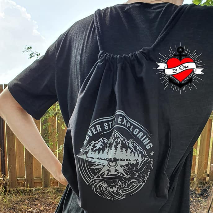 Eine Person trägt einen schwarzes Rucksack mit dem Design "NEVER STOP EXPLORING", das Teil der Plotterdatei von easy-sticks ist. Der Rucksack zeigt eine Berglandschaft und das inspirierende Motto, perfekt für kreative Projekte.