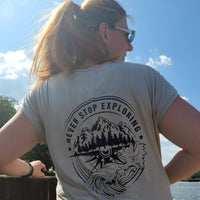 Junge Frau trägt ein T-Shirt mit dem Design "NEVER STOP EXPLORING" von easy-sticks, unterstrichen durch die beeindruckende Plotterdatei, während sie am Wasser steht.