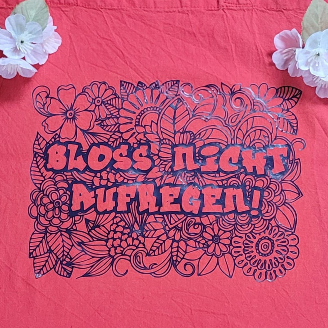 Tote Bag in leuchtendem Korallenrot mit dem Aufdruck 'Bloß nicht aufregen' von easy-sticks, umgeben von zwei zarten Blüten; perfekt für kreative DIY-Projekte.