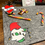 Nikolaus Wichtel Plotterdatei von easy-sticks, Wichtel auf einem grauen Filzuntergrund, umgeben von festlichem Süßigkeiten und Dekoration.