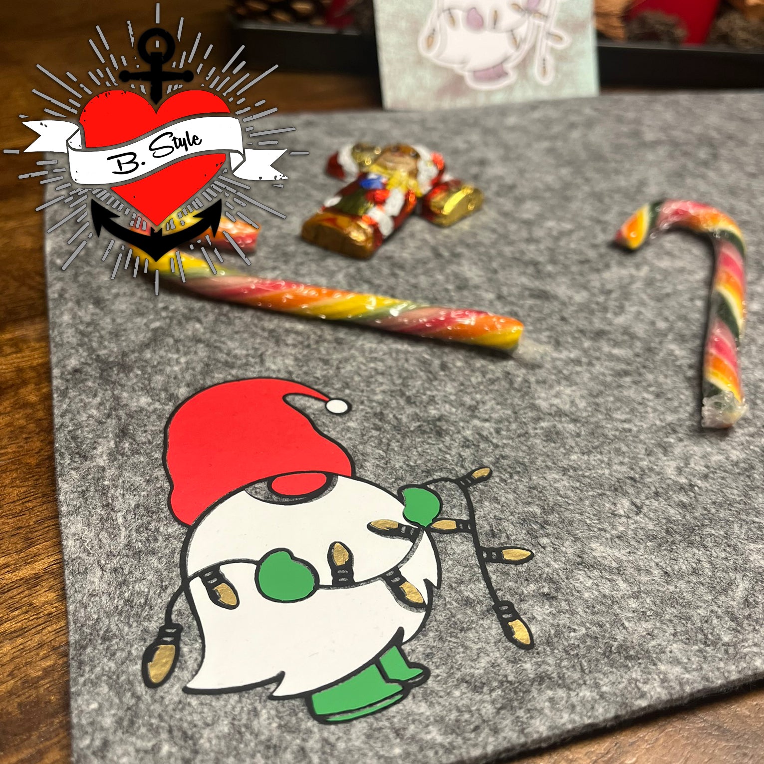 Nikolaus Wichtel Plotterdatei von easy-sticks, Wichtel auf einem grauen Filzuntergrund, umgeben von festlichem Süßigkeiten und Dekoration.