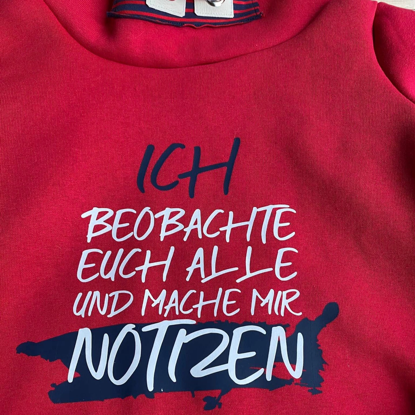 Stylisches rotes Sweatshirt mit dem Aufdruck "ICH BEOBACHTE EUCH ALLE UND MACHE MIR NOTIZEN", entworfen von easy-sticks, ideal für kreative DIY-Projekte.