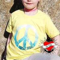 Ein Kind trägt ein gelbes T-Shirt mit einem blauen Peace-Symbol, inspiriert von der "PEACE" Grunge Schriftart Plotterdatei von easy-sticks. Perfekt für kreative DIY-Projekte! Plotterdatei.