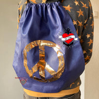 Rucksack mit 'PEACE' Grunge Schriftart Plotterdatei von easy-sticks, verziert mit einem glänzenden Friedenzeichen auf blauer Stoffoberfläche, ideal für kreative DIY-Projekte.