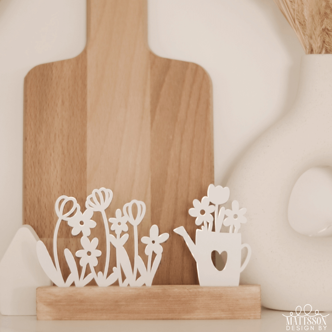 Dekorative Gießkanne und Blumenwiese aufsteller im minimalistischen Stil, von easy-sticks, perfekt für kreative Bastelprojekte und Heimdekoration. Gießkanne Plotterdatei und Blumenwiese Aufsteller zum Download.