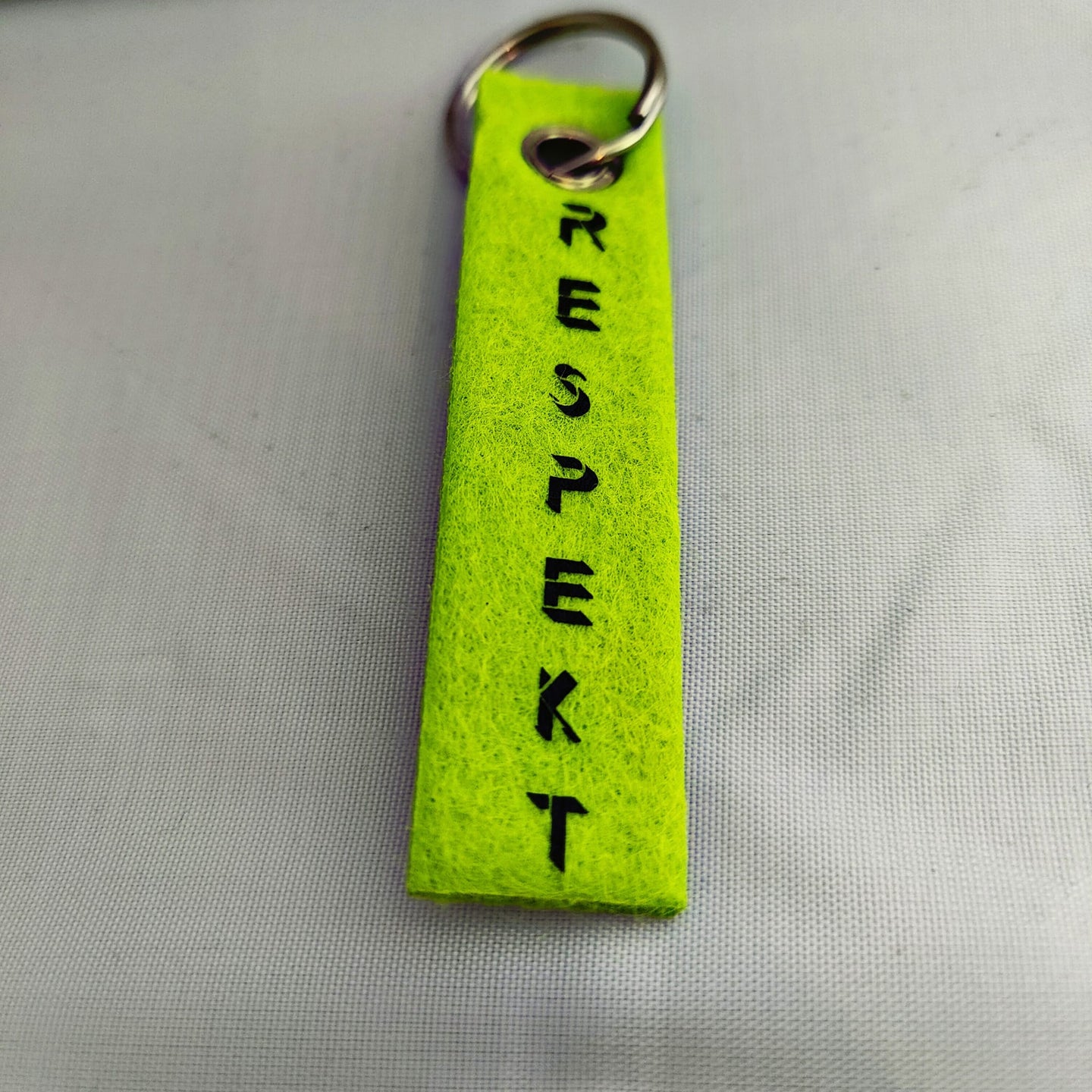 Ein leuchtend grüner Schlüsselanhänger, gestaltet mit der "Respekt" Plotterdatei von easy-sticks, der den Schriftzug "RESPEKT" in stilvoller Schrift trägt. Ideal für individuelle Designs und kreative Ideen.