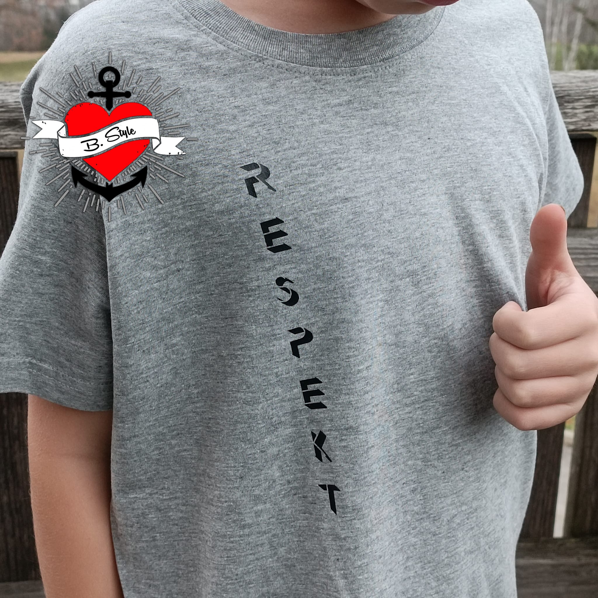 Ein Kind in einem grauen T-Shirt, das mit der "Respekt" Plotterdatei von easy-sticks personalisiert wurde, zeigt stolz den Schriftzug "RESPEKT". Perfekt für individuelle Mode.
