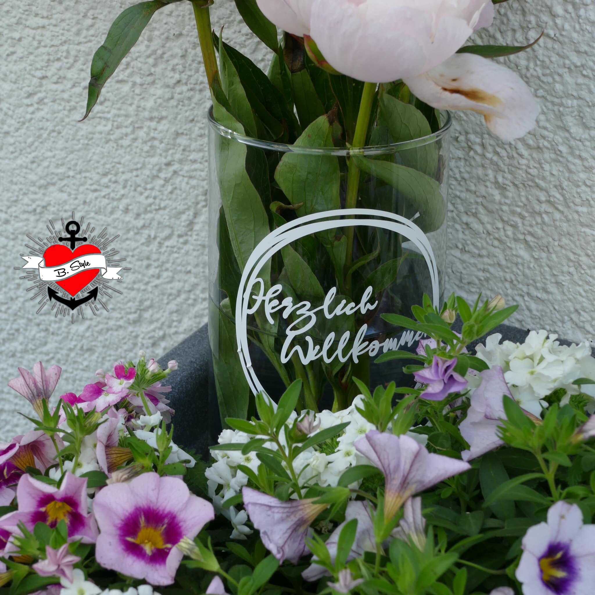 Vase mit dem Schriftzug 'Herzlich Willkommen', umgeben von bunten Gartenpflanzen, ein kreatives Produkt von easy-sticks, ideal für die Begrüßung von Gästen.