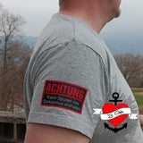 Seitenansicht eines grauen T-Shirts mit der Aufschrift "Achtung - Kann Spuren von Sarkasmus enthalten" von easy-sticks, das für humorvolle Statement-Kleidung steht.